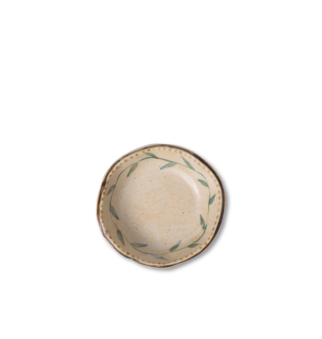 Overhead view of a round ceramic salt bowl with an organic rim, decorated with a green leafy vine border and a gold dotted accent line on a white background