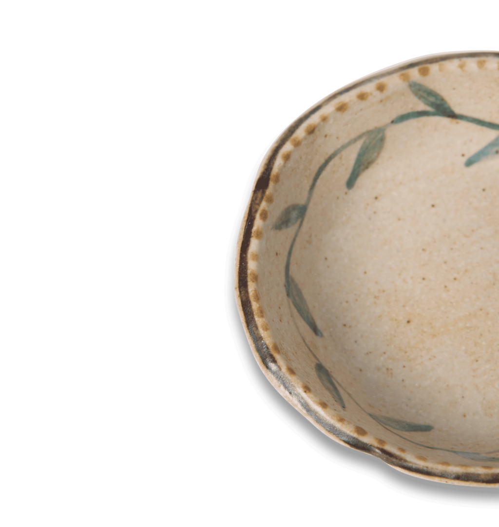 Detail view of a round ceramic salt bowl with an organic rim, decorated with a green leafy vine border and a gold dotted accent line on a white background