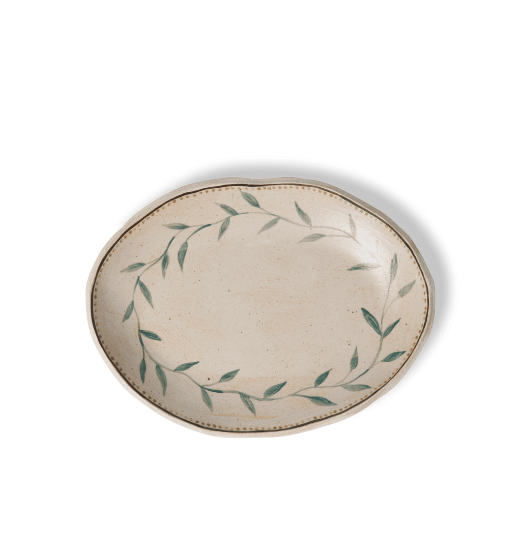 Overhead view of an oval ceramic serving platter with an organic rim, decorated with a green leafy vine border and a gold dotted accent line on a white background