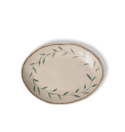 Overhead view of an oval ceramic serving platter with an organic rim, decorated with a green leafy vine border and a gold dotted accent line on a white background