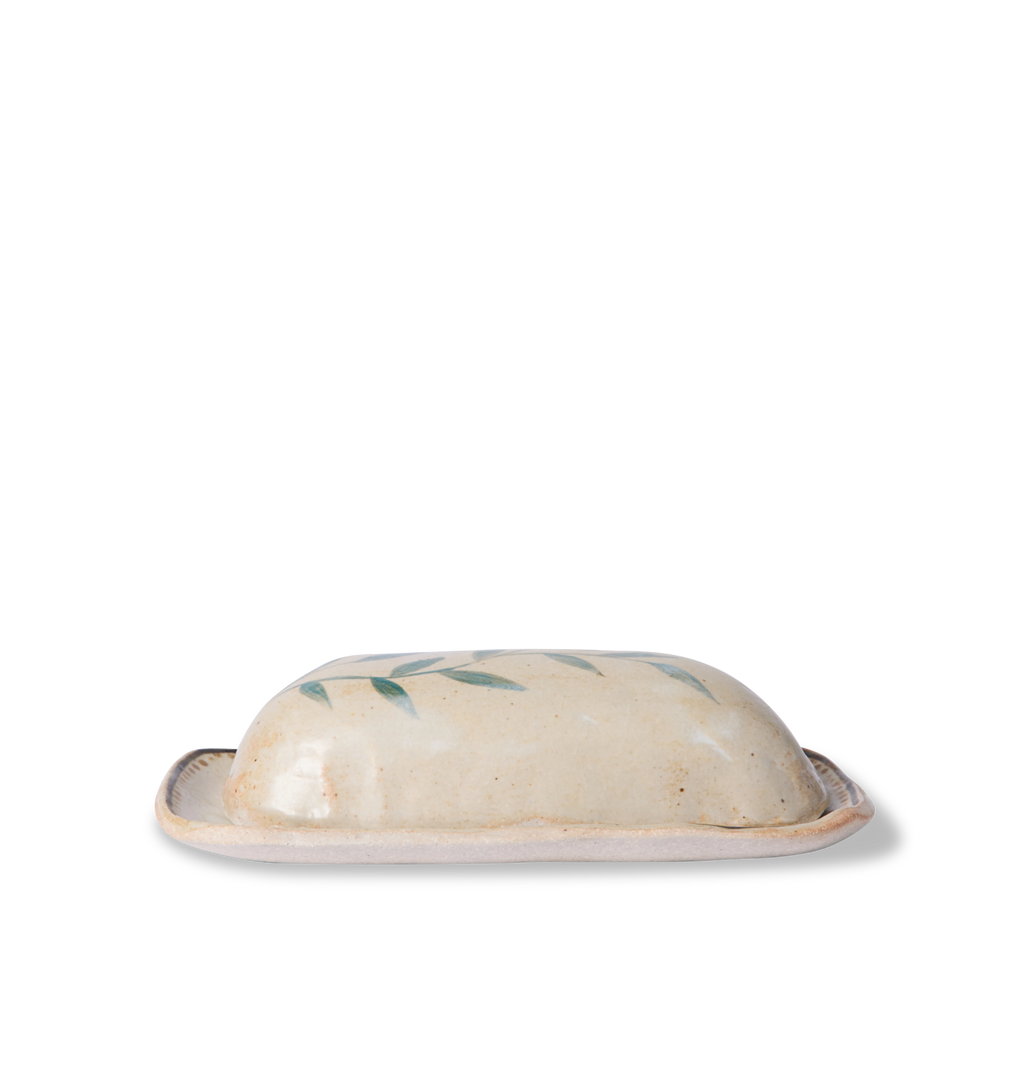 Side view of a ceramic butter dish and lid decorated with a green leafy vine border and a gold dotted accent line on a white background