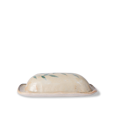 Side view of a ceramic butter dish and lid decorated with a green leafy vine border and a gold dotted accent line on a white background
