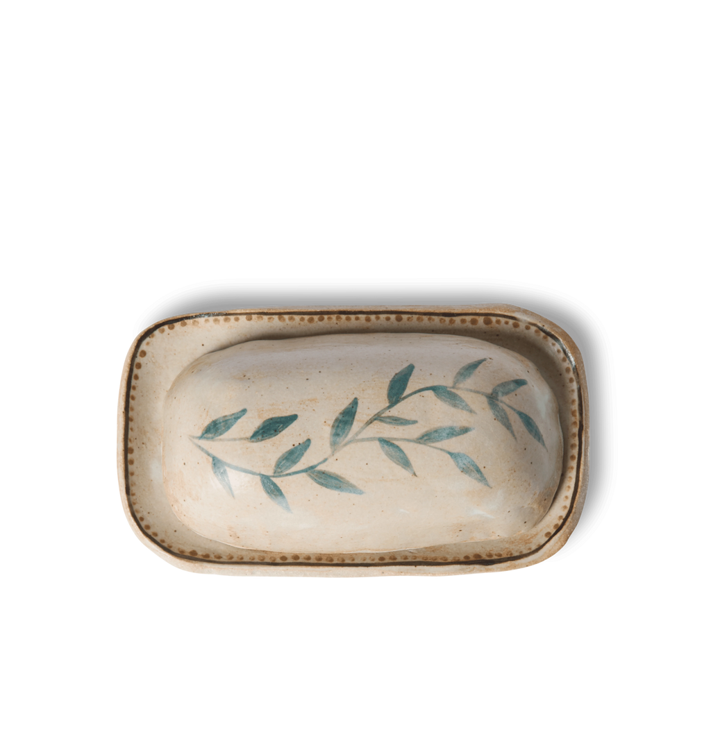 Overhead view of a ceramic butter dish and lid decorated with a green leafy vine border and a gold dotted accent line on a white background
