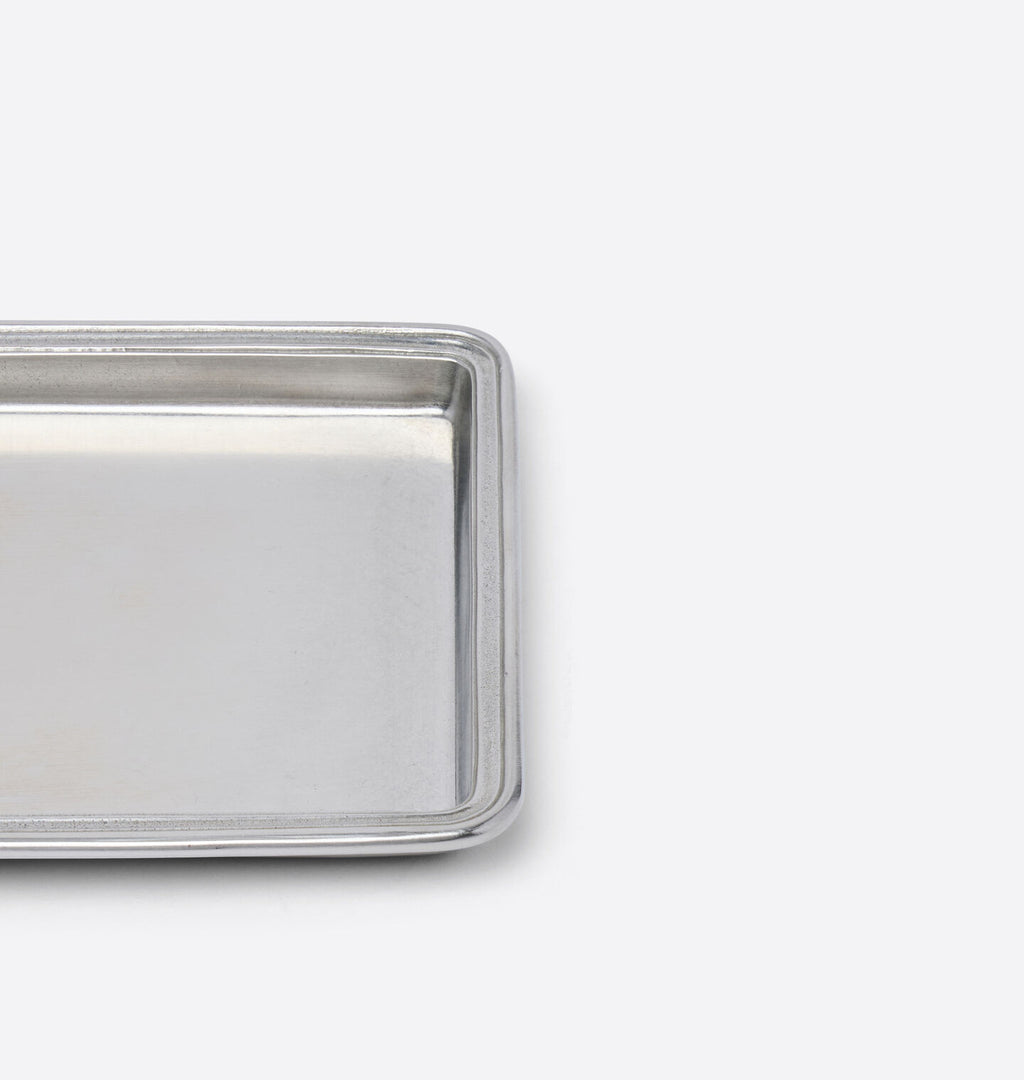 A close-up of a rectangular pewter vanity tray, cropped on the left side against a clean white background.