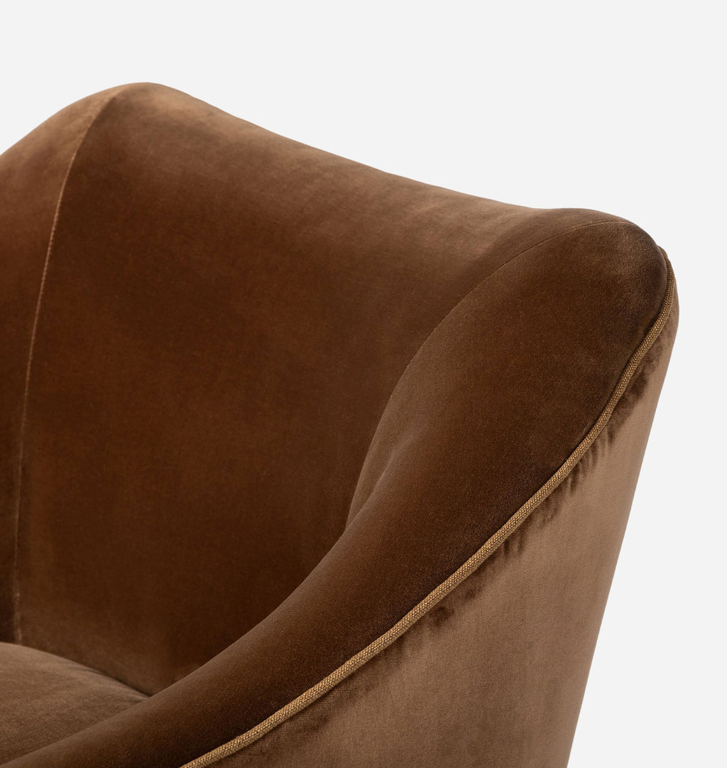 Close-up of a brown velvet upholstered armchair showing the curved backrest and arm with a thin contrasting piping detail, set against a plain light gray background.