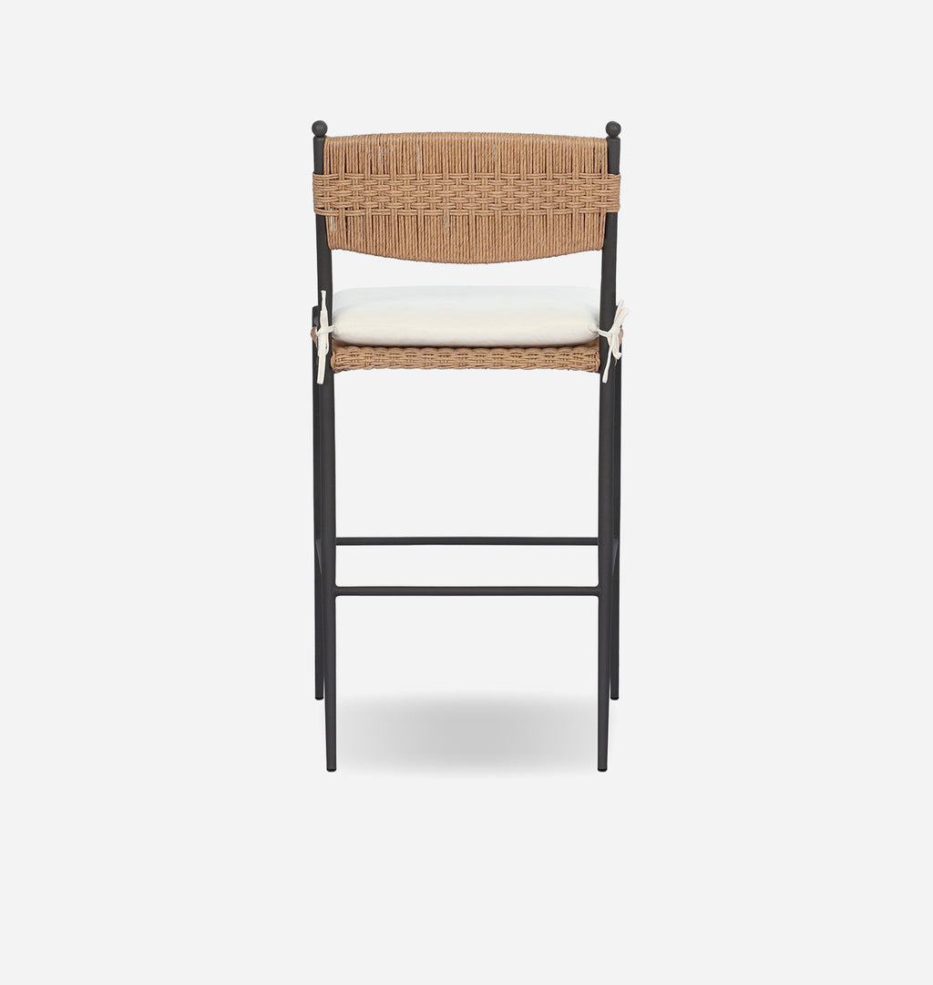 A modern outdoor bar stool with a black metal frame, woven natural backrest and seat, and a white cushion, shown against a light gray background.