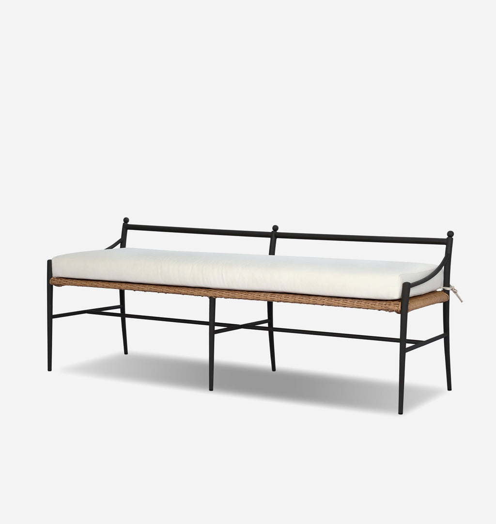 A modern outdoor bench with a black metal frame, a natural woven rattan seat, and a thick off-white cushion, shown against a light gray background.