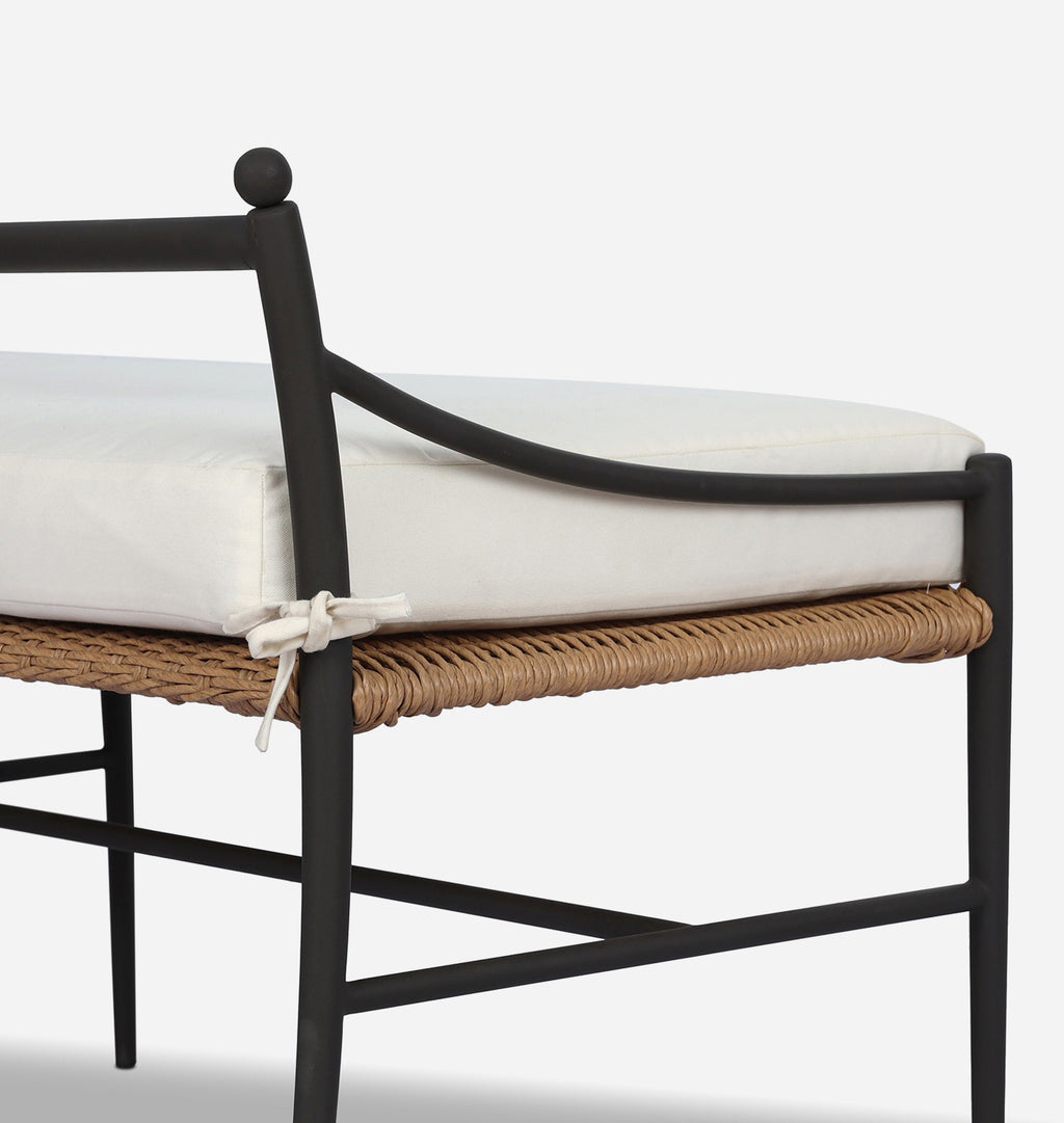 Outdoor bench with a black metal frame, woven wicker seat, and a thick white cushion tied with a small white bow.