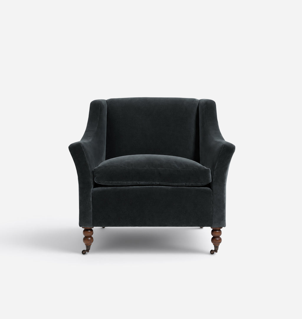 A dark charcoal navy velvet armchair with turned wooden legs, shown from the front against a light gray background.