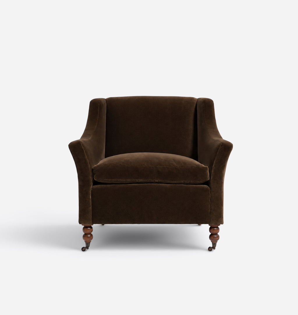 A classic wingback armchair upholstered in dark brown velvet, featuring turned wooden legs and a matching seat cushion, set against a plain light gray background.