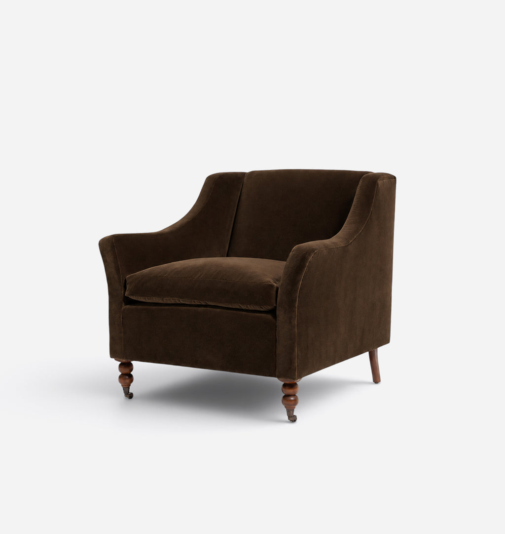 A classic brown velvet armchair with a high curved backrest, wide armrests, and turned wooden legs, shown on a plain light gray background.
