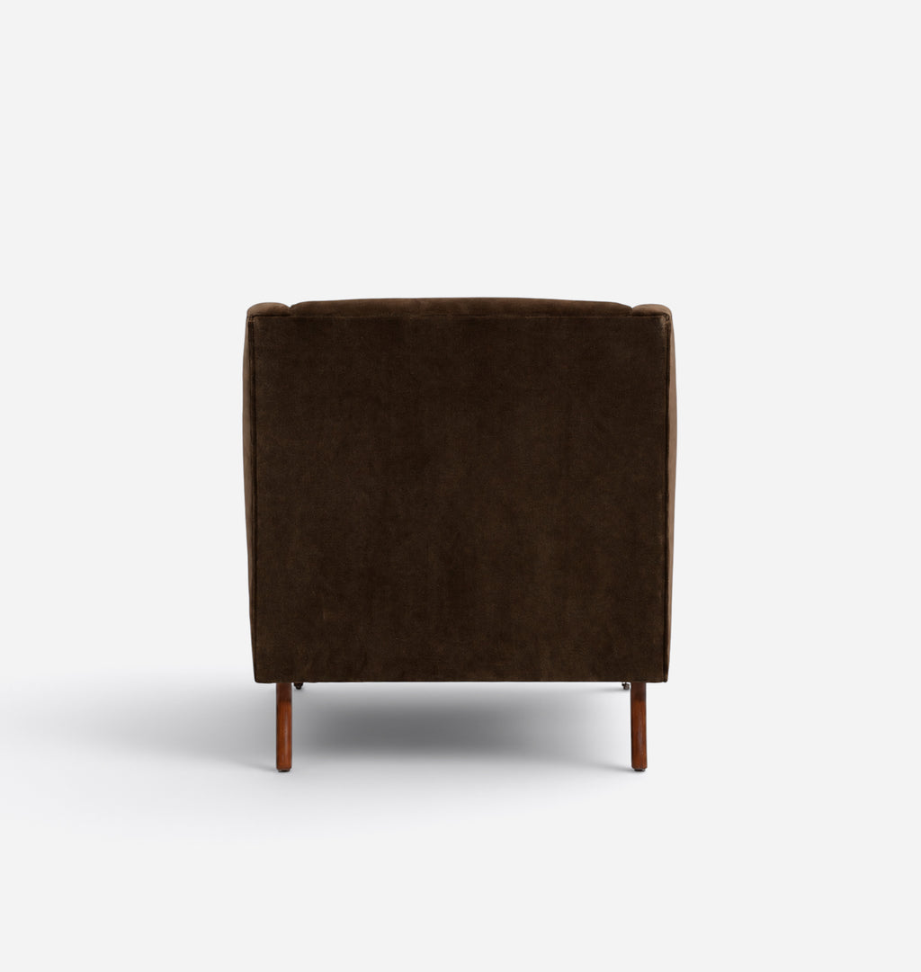 A dark brown velvet armchair shown from the back, featuring a square backrest and tapered wooden legs, set against a plain white studio background.
