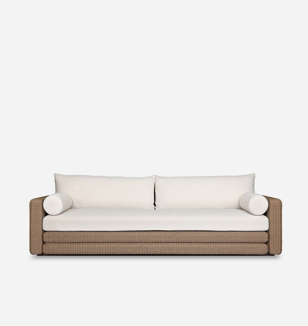 A modern outdoor sofa with a textured brown woven frame and thick off-white cushions, including two back cushions and two cylindrical bolsters, shown against a plain white background.