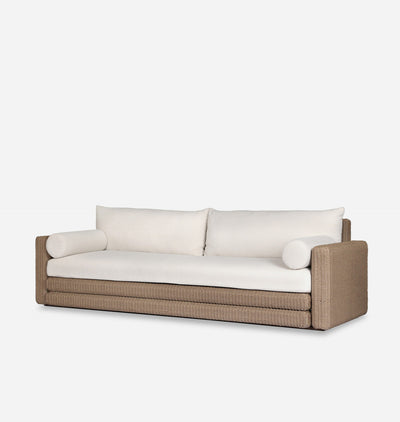 A modern outdoor sofa with a woven wicker frame in a warm taupe-brown color and thick, plush off-white cushions, shown against a plain light gray background.