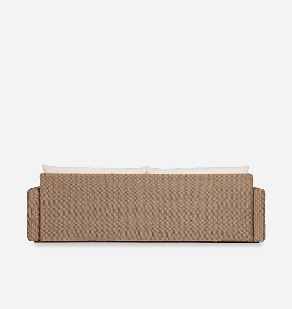 A low-profile outdoor sofa viewed from the back, featuring a textured beige woven frame and two cream-colored back cushions, set against a solid white background.