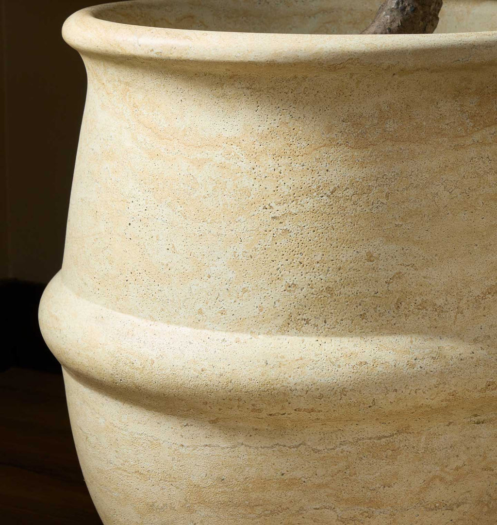 Close-up of a large textured stone planter pot in a warm beige color, showing its rustic speckled surface and curved rim.