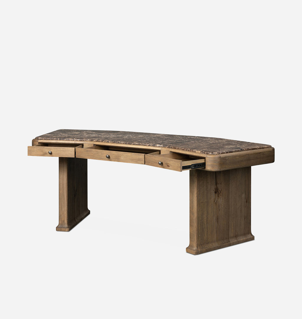 A rustic wooden writing desk with a curved top, featuring a dark textured inlay, three drawers on the front with one open to reveal storage space, and two block-style legs. The desk is shown on a plain light gray background.