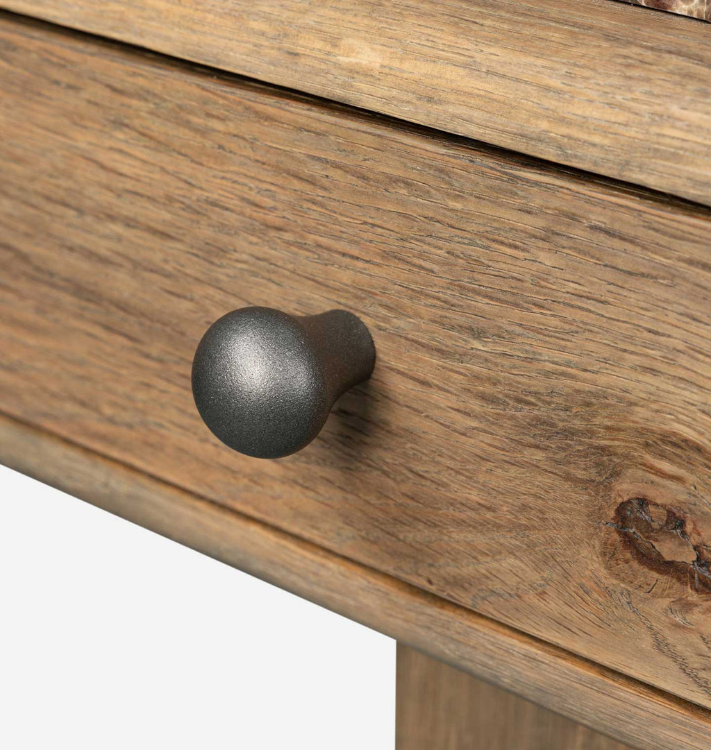 A close-up of a medium brown wooden drawer front with a round matte black metal knob, set against a white background.