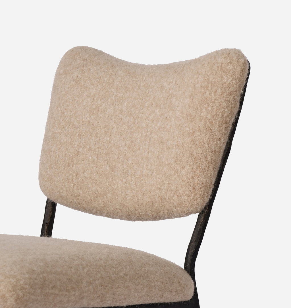 Close-up of a chair with a textured beige bouclé upholstered backrest and seat, supported by a black metal frame, on a light gray background.