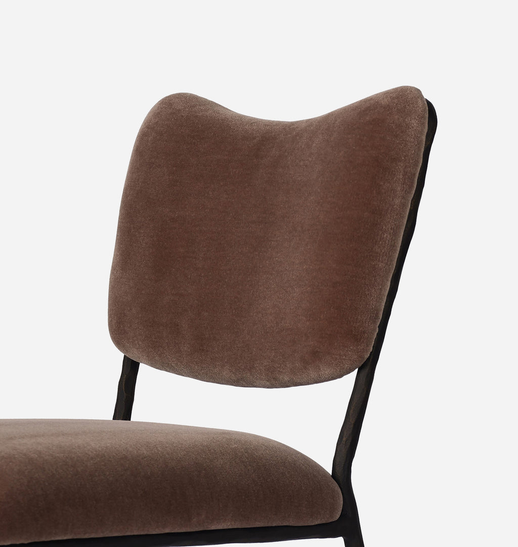 A close-up of a modern dining chair featuring a curved, cushioned backrest and seat upholstered in a textured brown velvet fabric, supported by slim black metal legs, set against a plain white background.