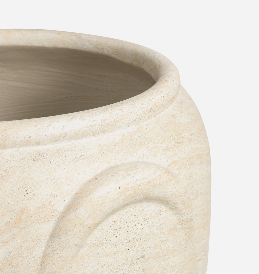 Close-up detail of a textured stone planter in a warm cream or beige color, showing the curved rim and a recessed decorative panel on the side against a plain white background.