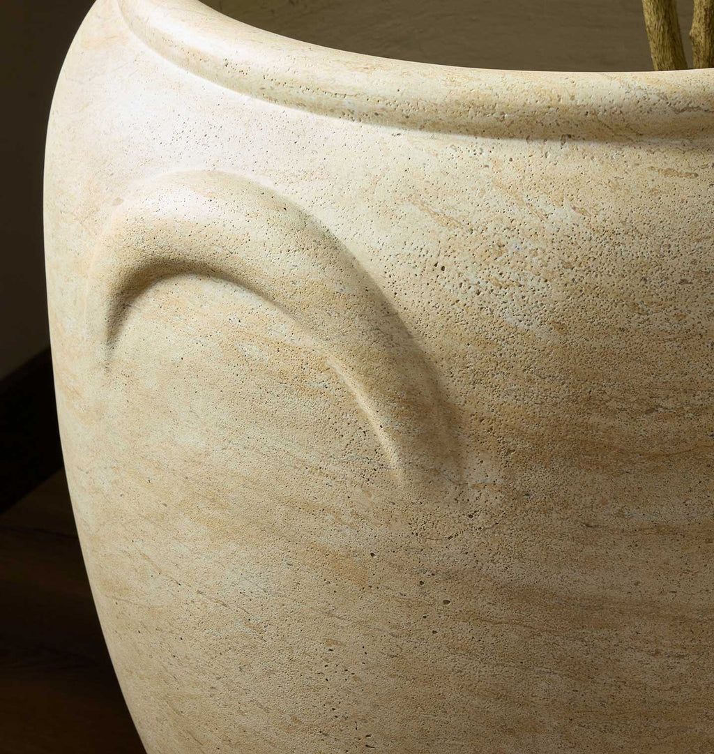 Close-up of a large textured ceramic planter pot in a warm beige stone-like finish, showing a curved recessed detail on the side.