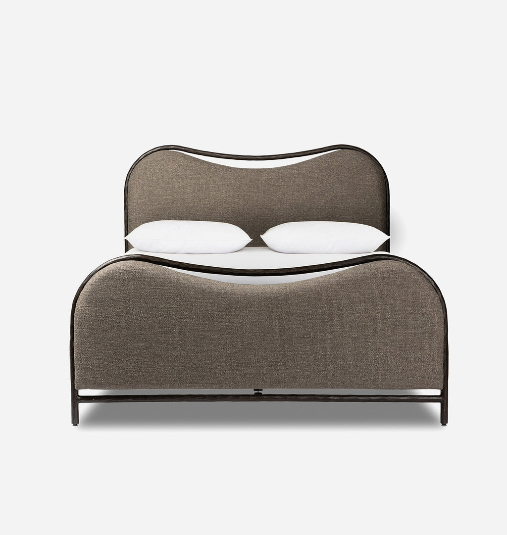 A modern low-profile bed with a curved upholstered headboard and footboard in taupe fabric, supported by a dark metal frame, shown with two white pillows on a light gray background.