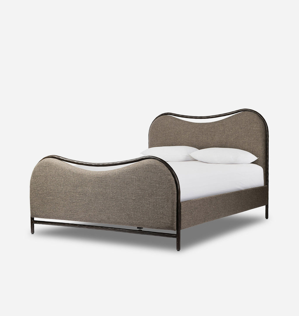 A modern curved bed frame with upholstered taupe fabric and a dark metal frame, shown with white bedding and pillows on a clean white background.