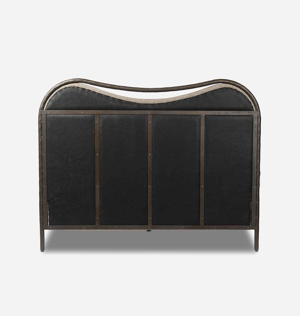A vintage-style upholstered headboard with a curved top, featuring black fabric panels and a weathered bronze metal frame, shown against a light gray background.