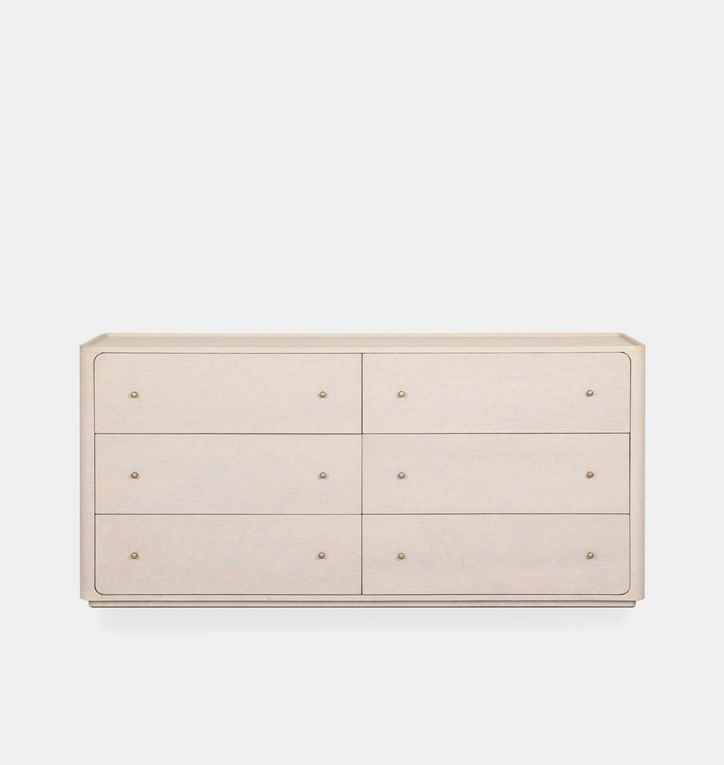 A light beige six-drawer dresser with small round metallic knobs, shown against a plain light gray background.