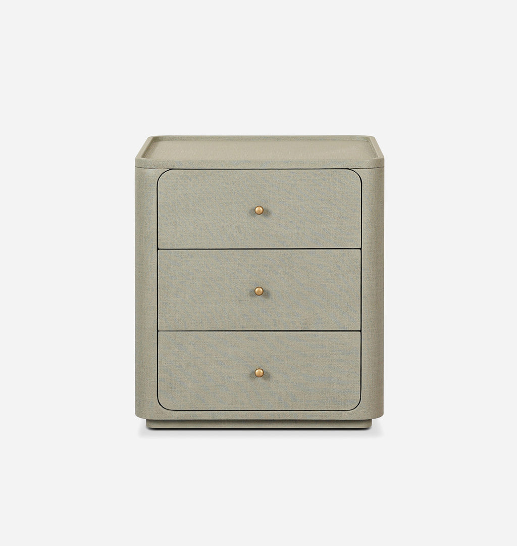 A three-drawer nightstand in a textured light gray fabric, featuring small round brass knobs and a matching top surface, shown against a plain white background.