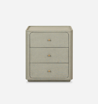A three-drawer nightstand in a textured light gray fabric, featuring small round brass knobs and a matching top surface, shown against a plain white background.