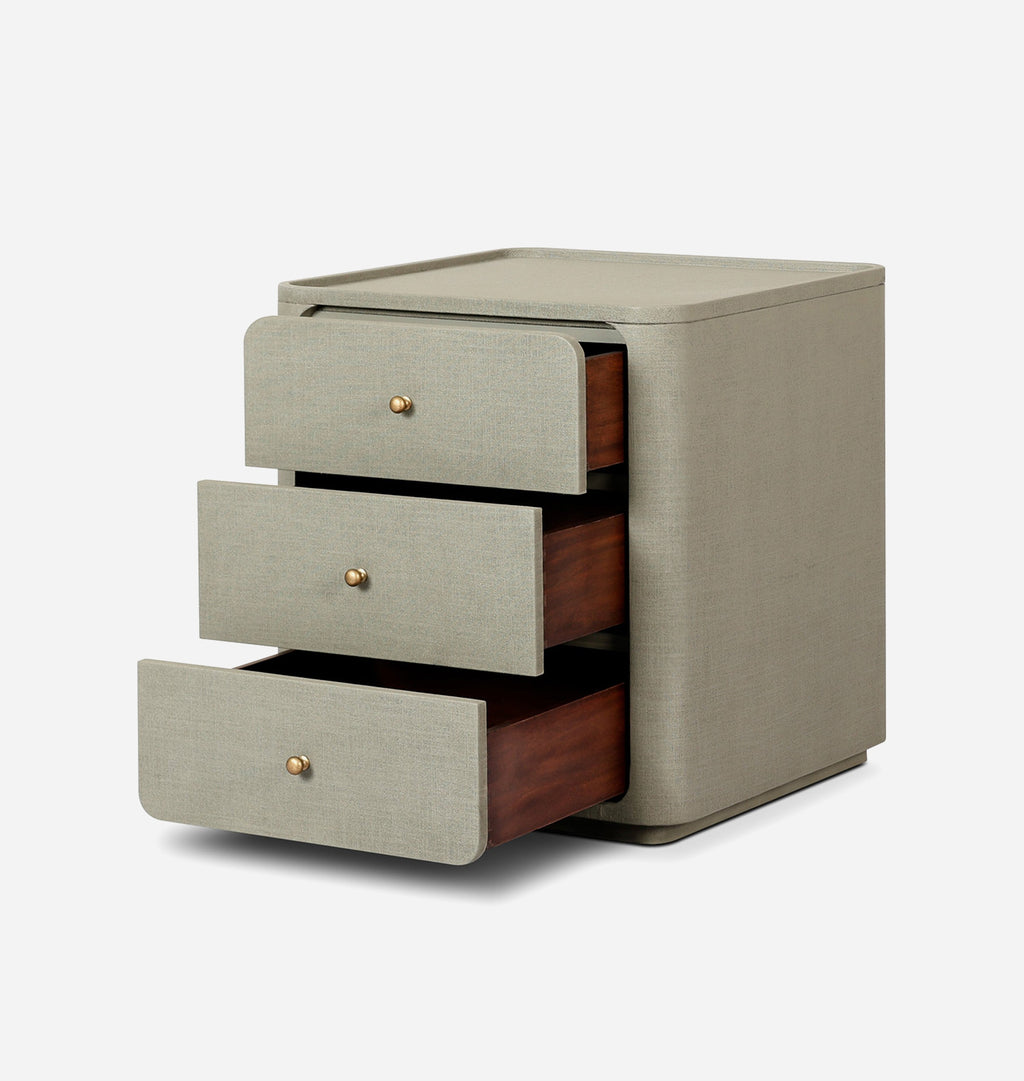 A modern three-drawer nightstand with a textured light beige linen fabric exterior and dark brown wood interiors, featuring small round brass knobs, shown on a light gray background.