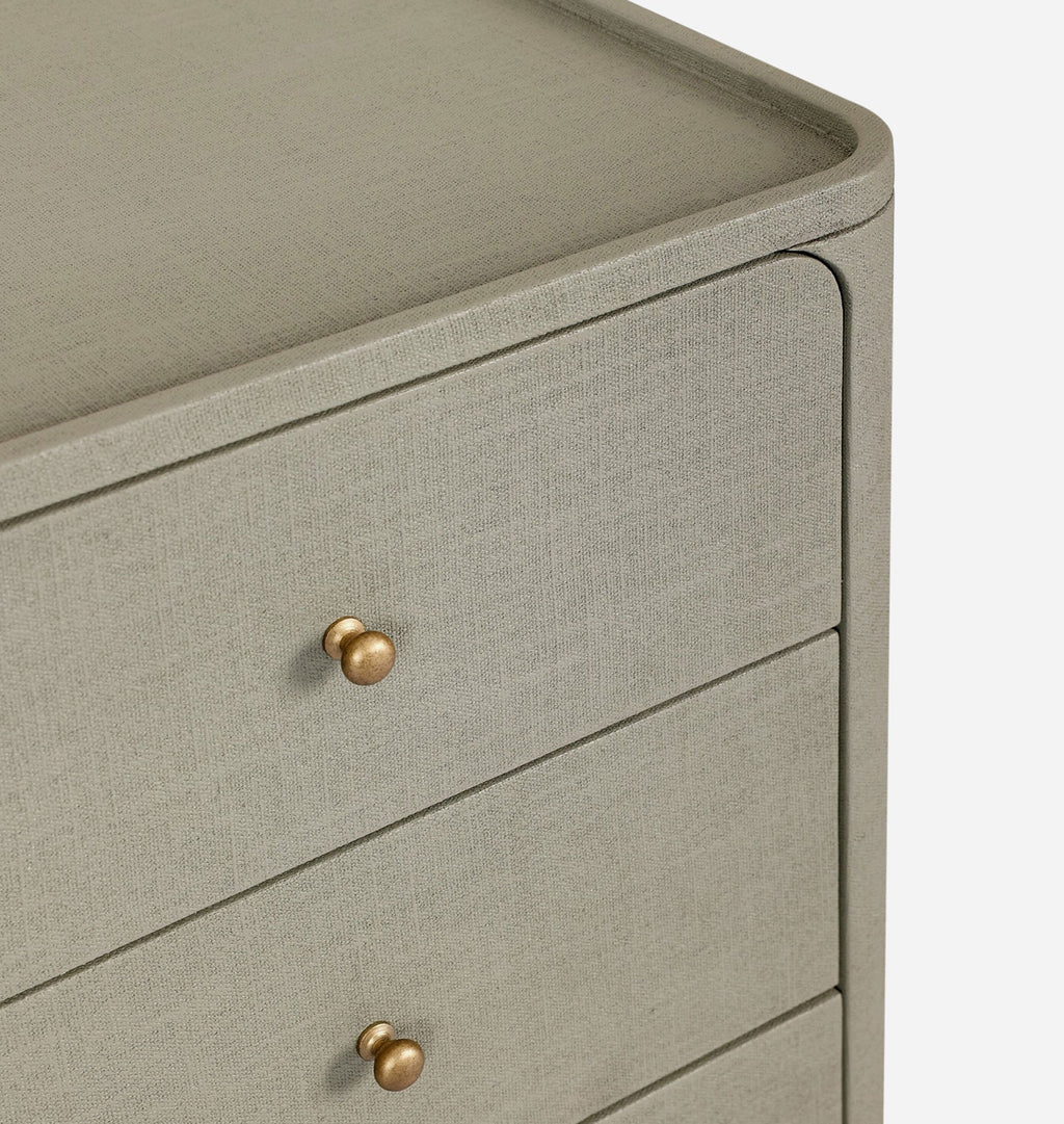 Close-up of a light gray linen-textured chest of drawers with two drawers and round brass knobs, set against a clean white background.
