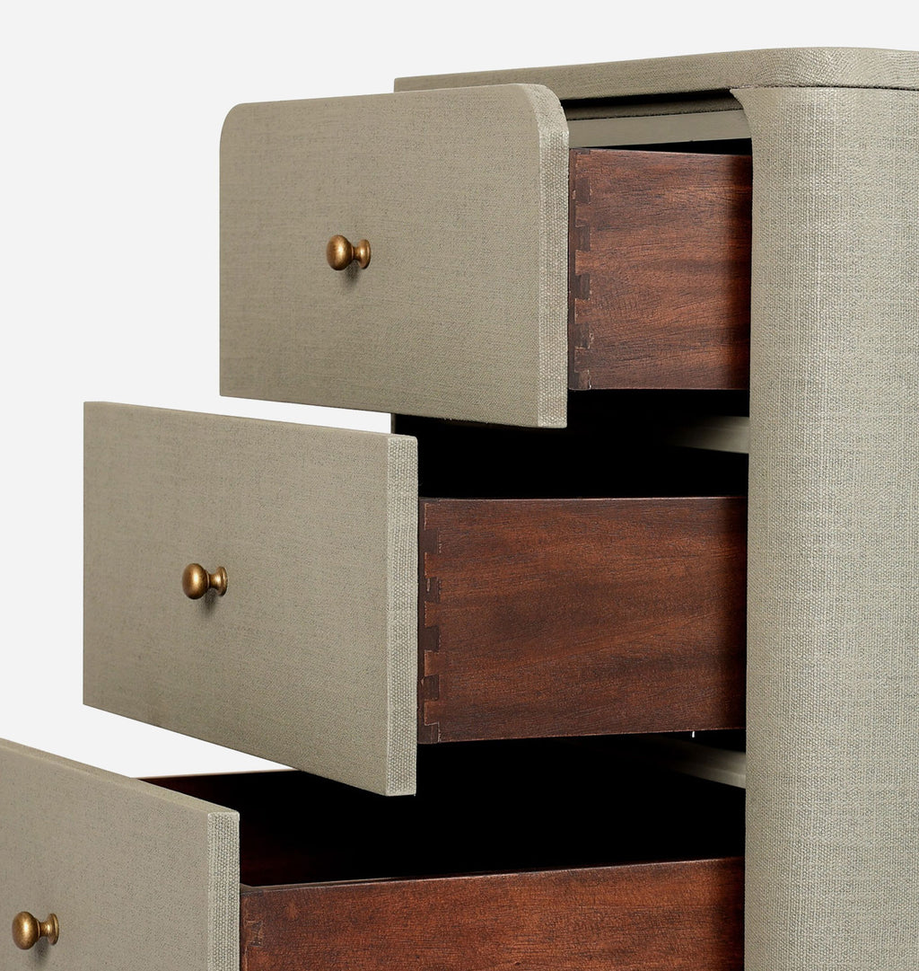 Close-up of a three-drawer chest or cabinet with light beige linen-covered fronts, brass round knobs, and dark reddish-brown wood drawer interiors, shown against a plain white background.