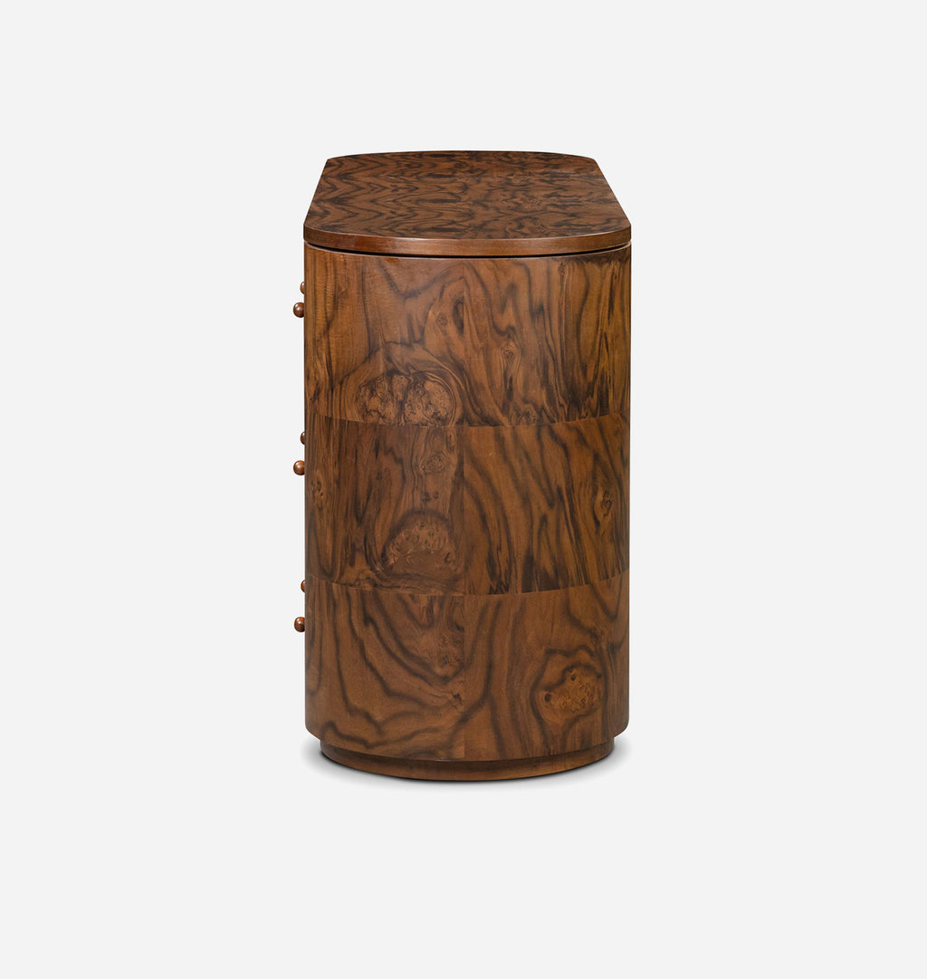 A vintage wooden sideboard or cabinet with a rounded top, featuring three drawers on the left with brass knobs and a rich burl wood grain pattern, shown against a plain light gray background.