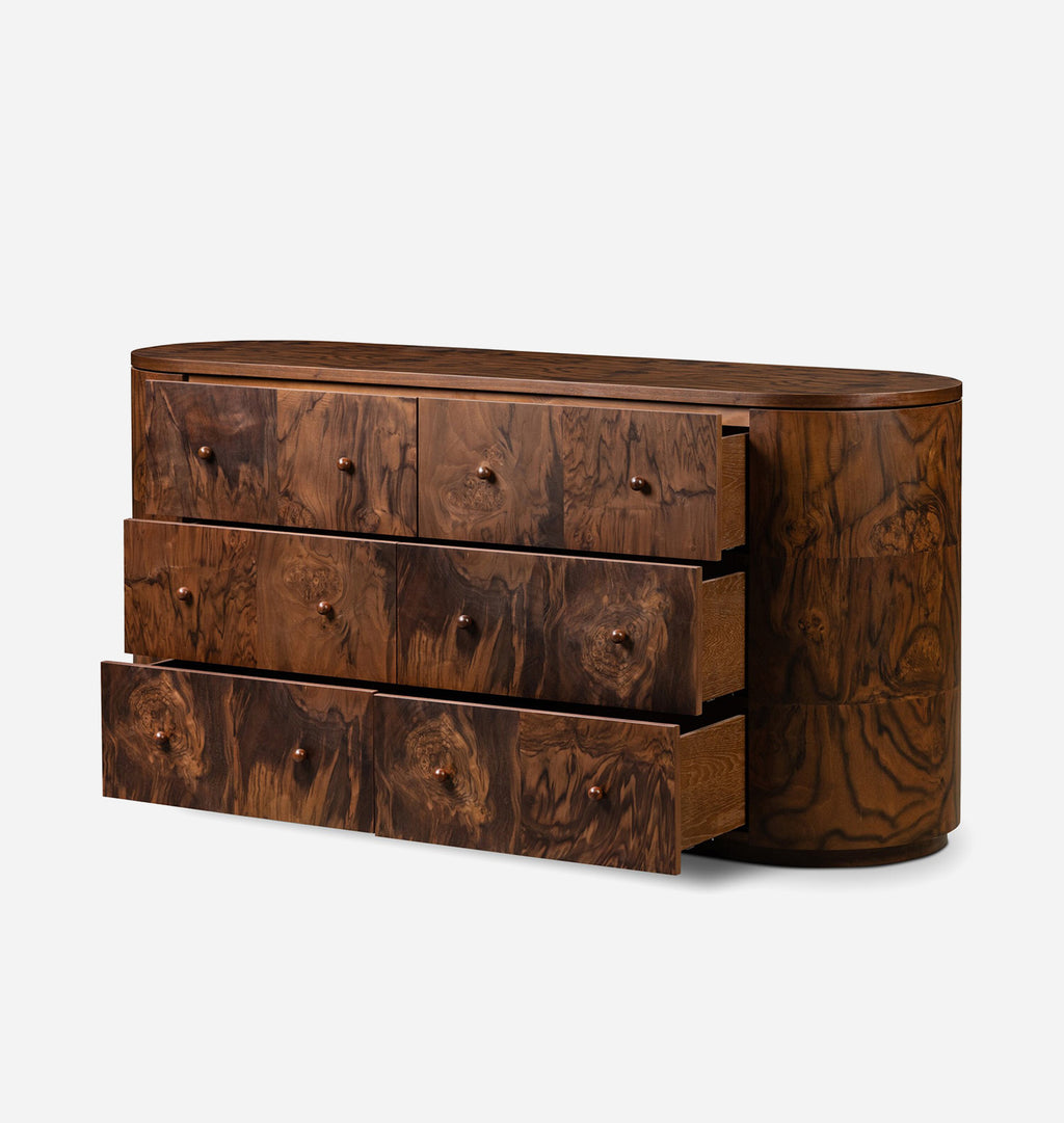 An oval-shaped wooden dresser with three drawers pulled out, showcasing rich, swirling burl wood grain in dark brown tones, set against a plain light gray background.