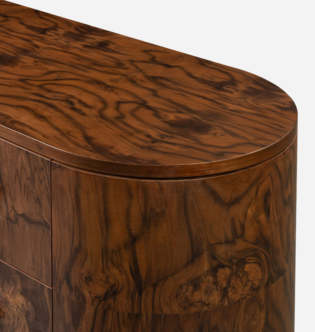 Close-up of a richly carved wooden cabinet or sideboard with a curved top, featuring dramatic dark brown and amber wood grain patterns on a light gray background.