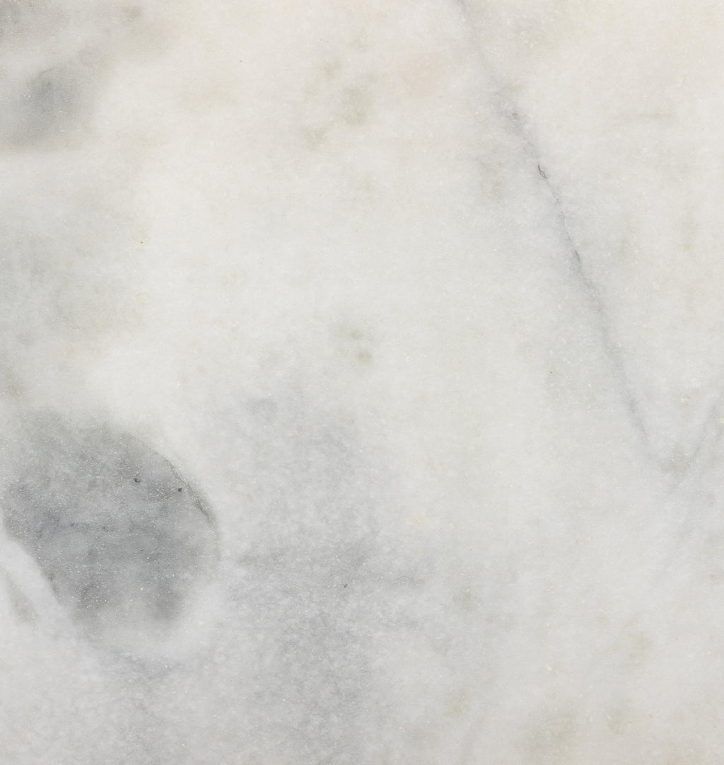 A close-up of a light marble or stone surface with soft white, gray, and faint beige veining and mottled texture.