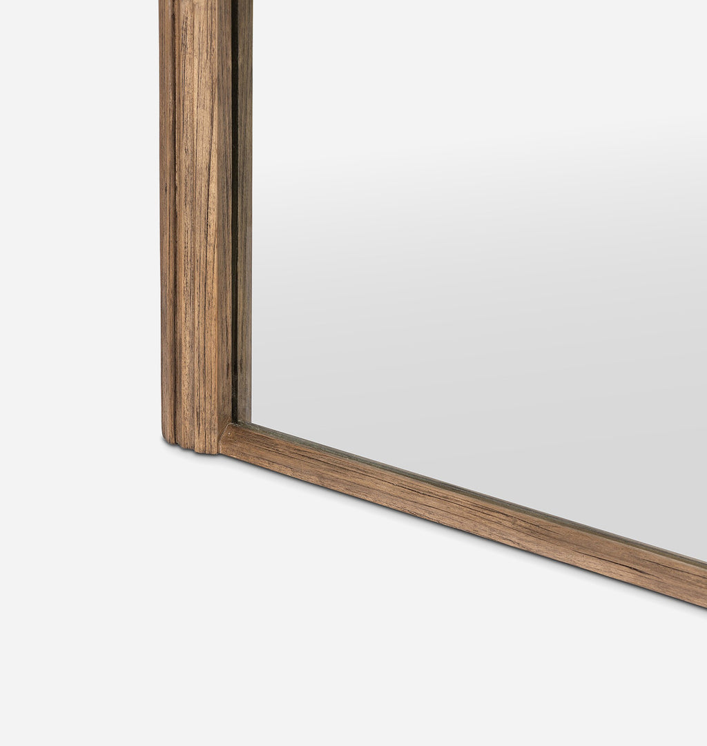 Close-up of the corner of a wall mirror with a medium brown wood grain frame on a light gray background.