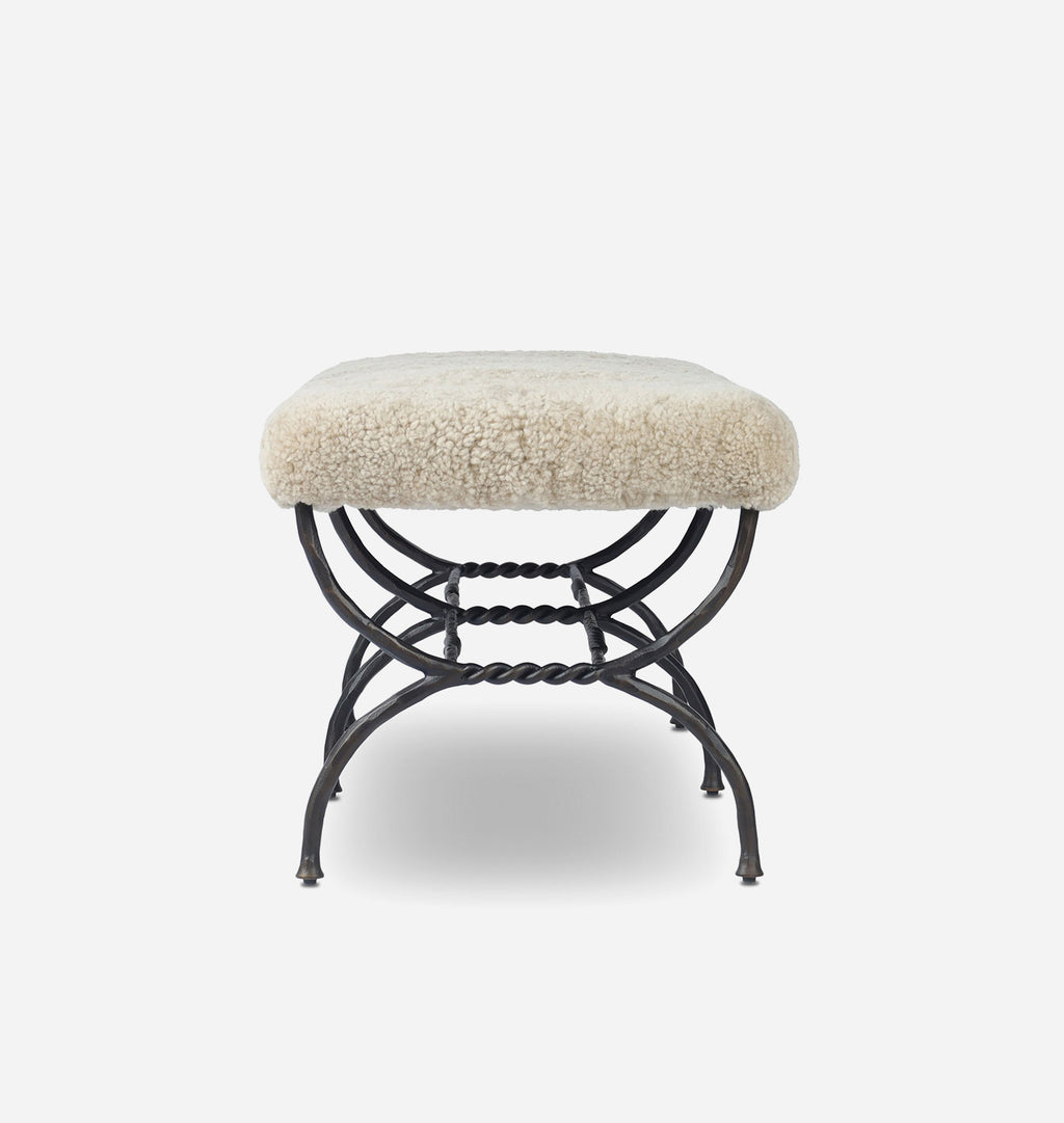 A square bench with a cream-colored sheepskin seat and a black metal frame with twisted decorative details, shown against a plain light gray background.