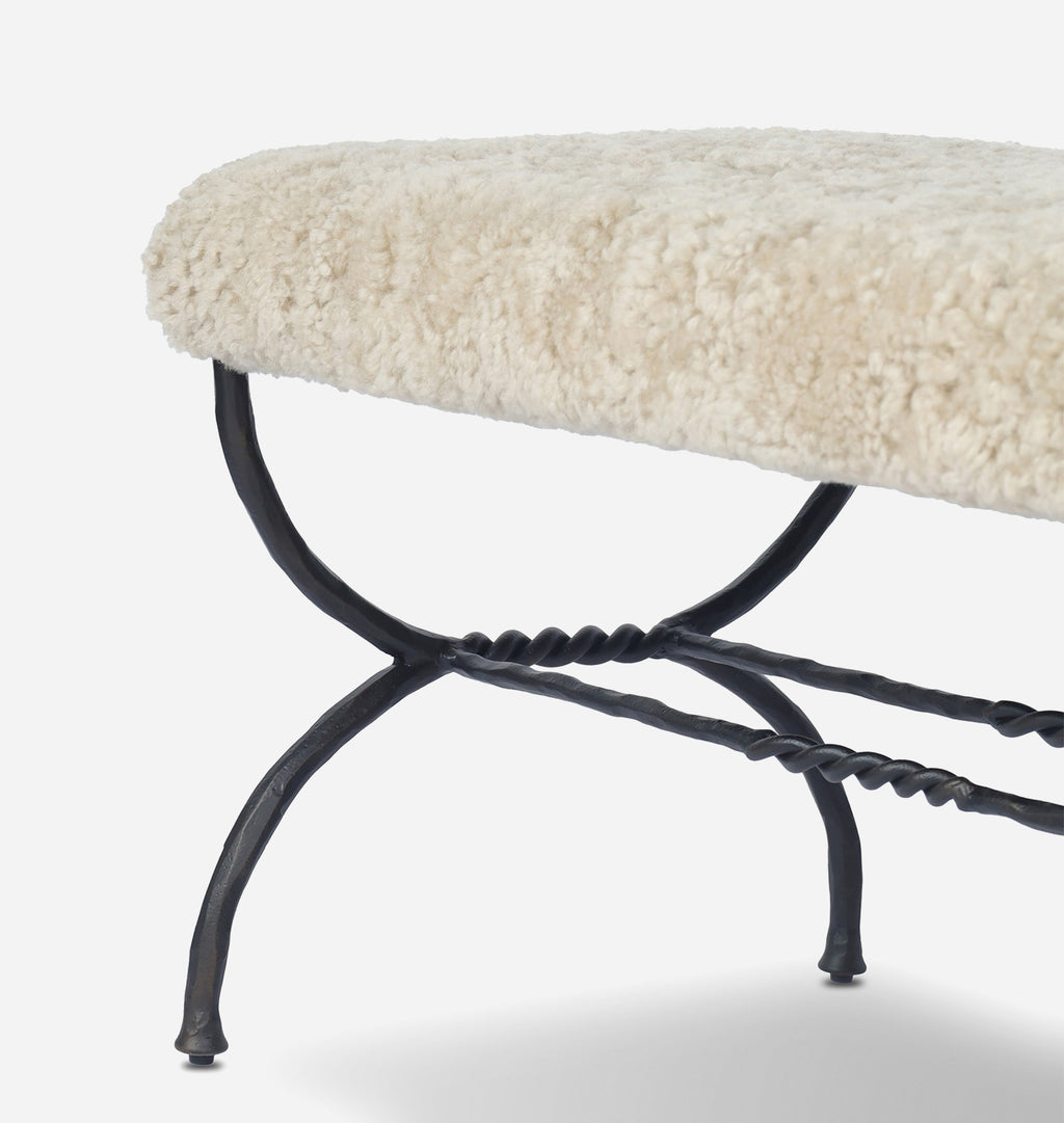 A close-up of a bench with a cream-colored sheepskin cushion and a black metal frame with twisted decorative details.