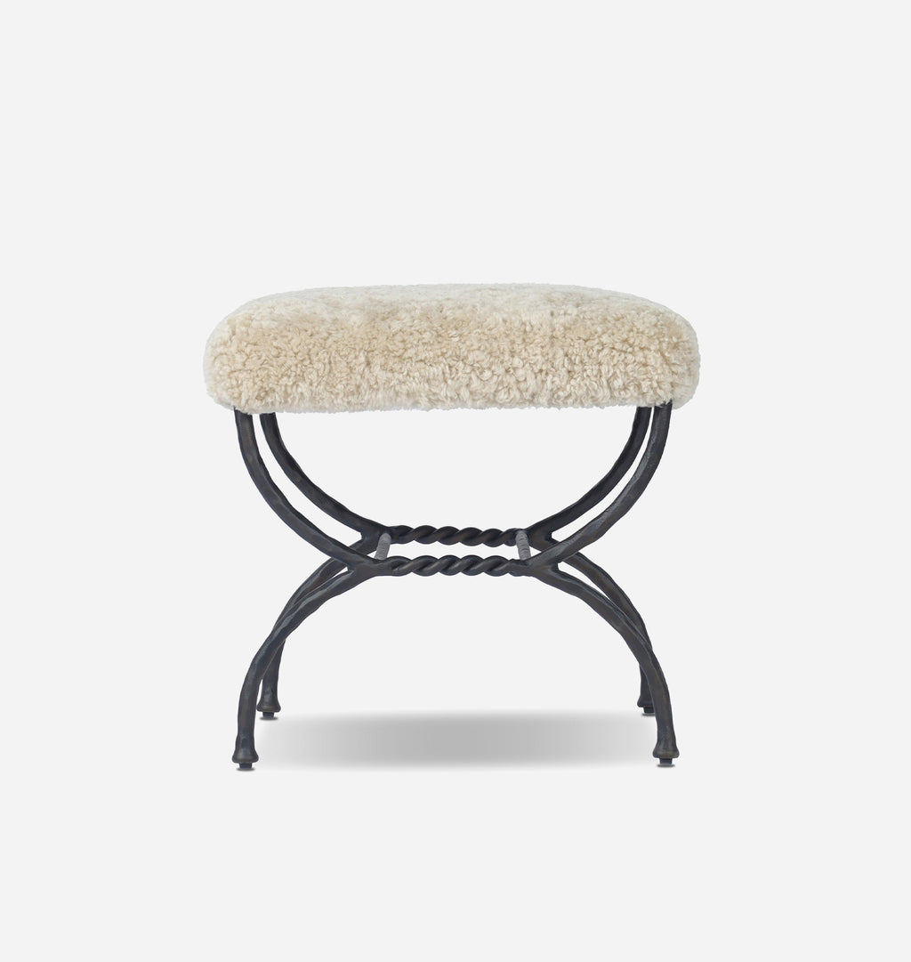 A small bench with a cream-colored shaggy sheepskin cushion on a black metal frame, shown against a plain light gray background.