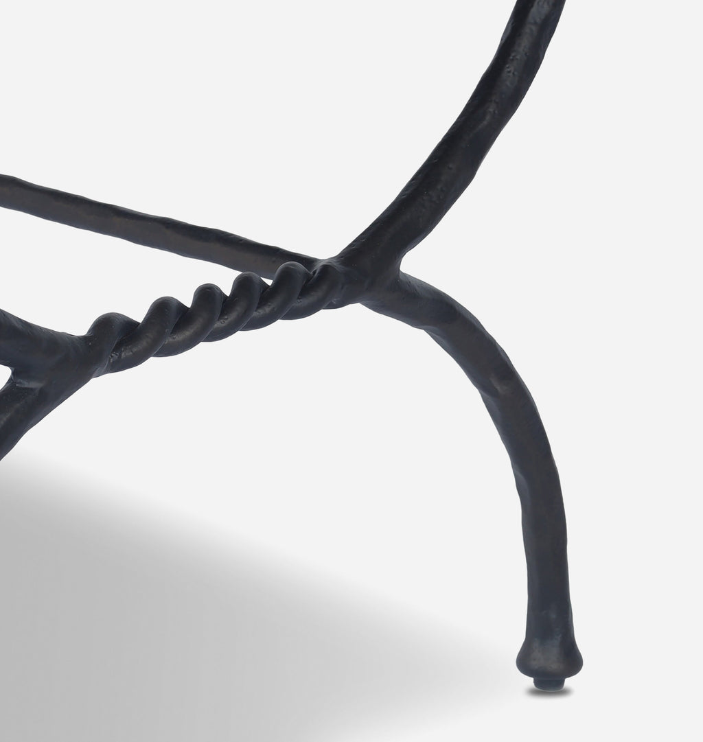 Close-up of a sculptural black metal chair leg with a twisted rope detail and curved armrest, photographed against a clean white background.
