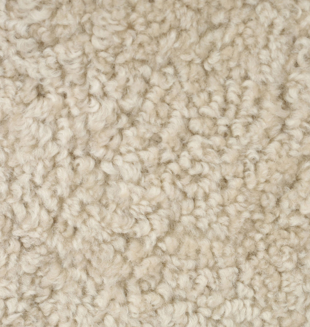 A close-up texture shot of a thick sheepskin in a warm cream or off-white color.