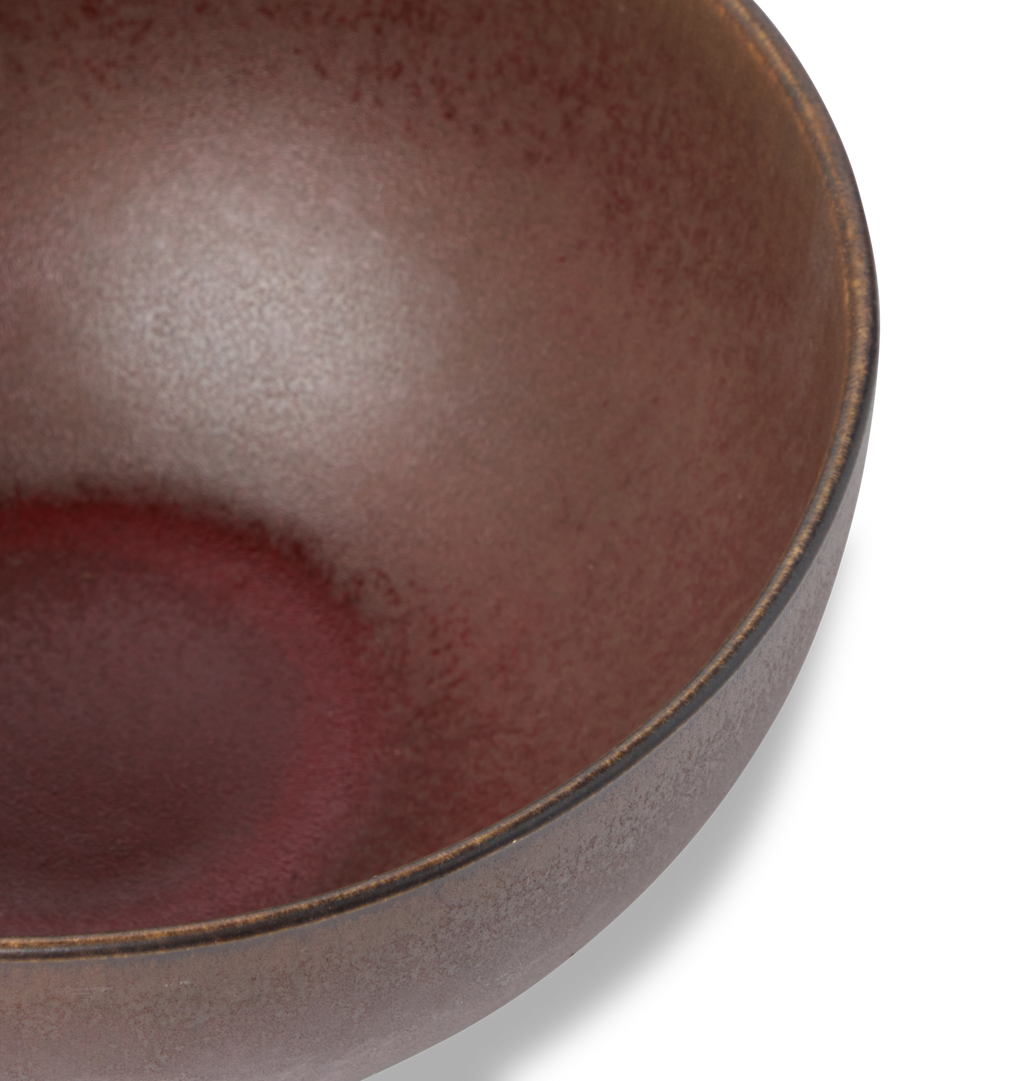 An overhead view of a ceramic pasta bowl finished in a reddish brown glaze shown on a white background
