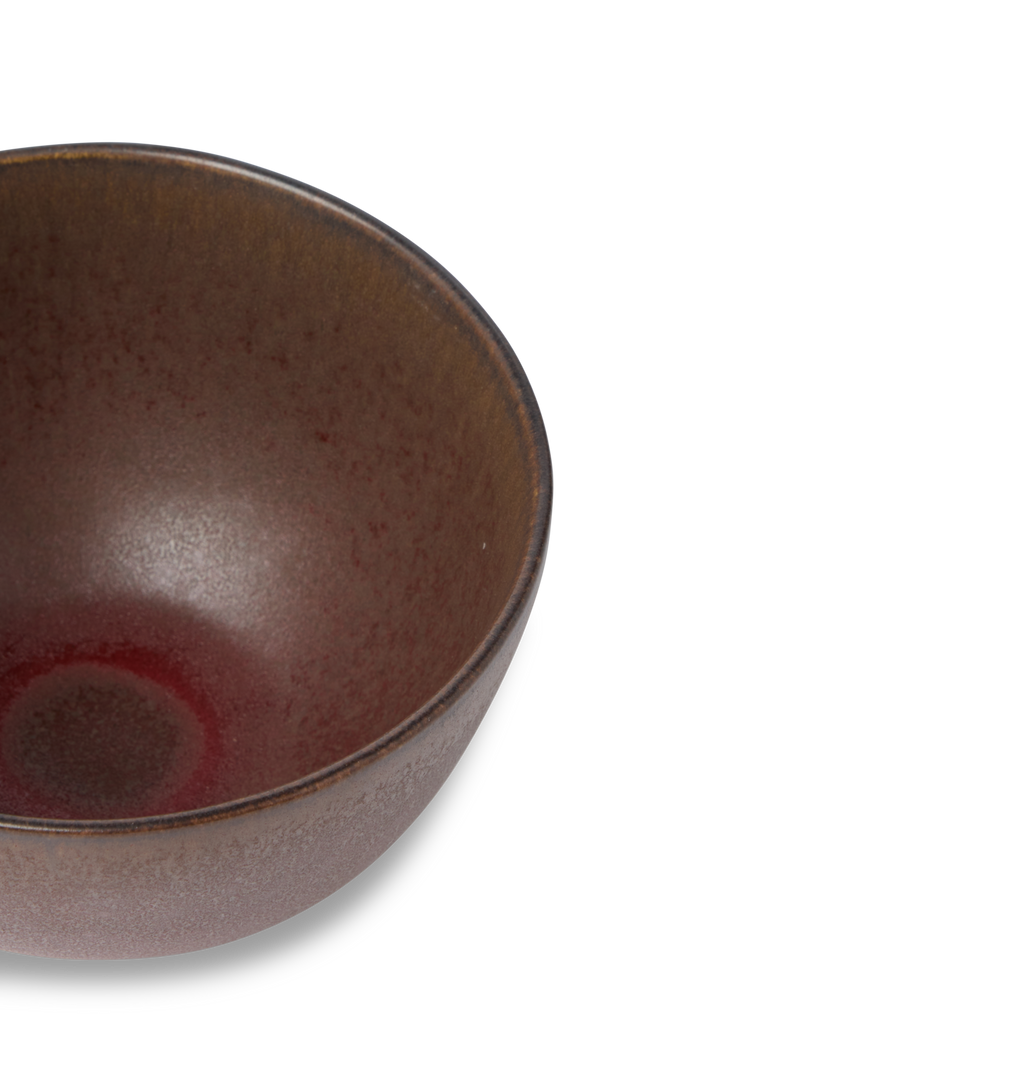 An overhead view of a ceramic cereal bowl finished in a reddish brown glaze shown on a white background