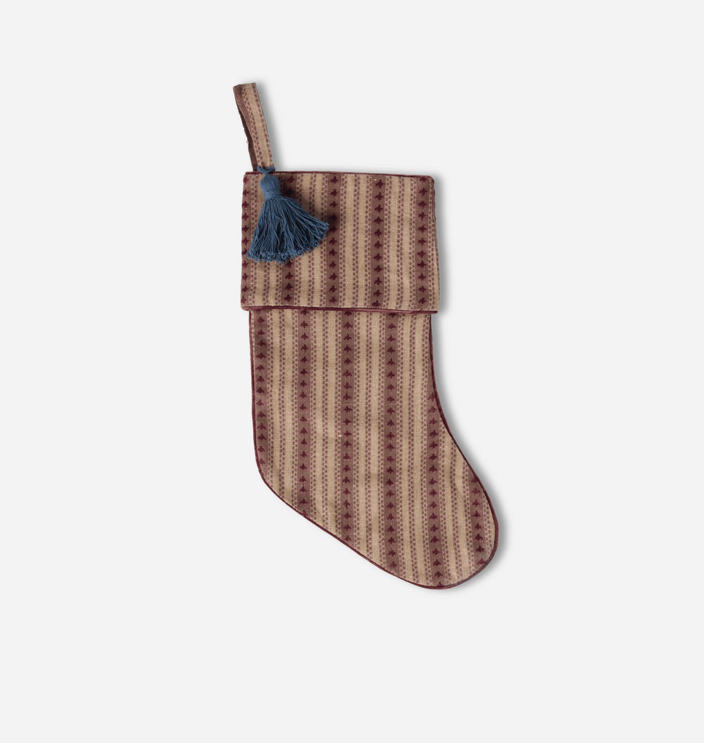 A patterned Christmas stocking with a brown and beige geometric design and a dark blue tassel, shown against a light gray background.