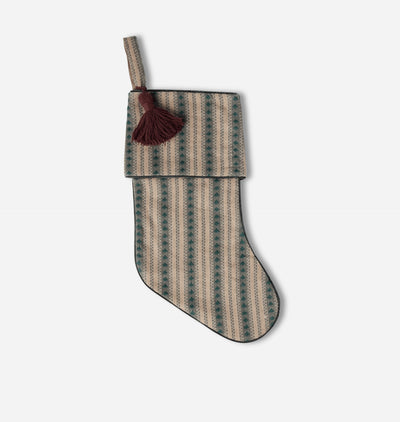 A knit Christmas stocking with vertical stripes in beige and dark green, featuring a dark brown tassel on a light gray background.