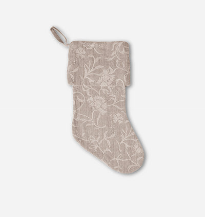 A single fabric Christmas stocking in a warm taupe-beige color with an intricate white floral embroidery pattern, shown against a plain light gray background.